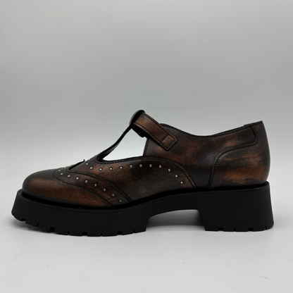 A single brown distressed leather T-strap Mary Jane shoe with silver stud detailing and a black chunky lug sole, shown from a side profile on a light gray background.