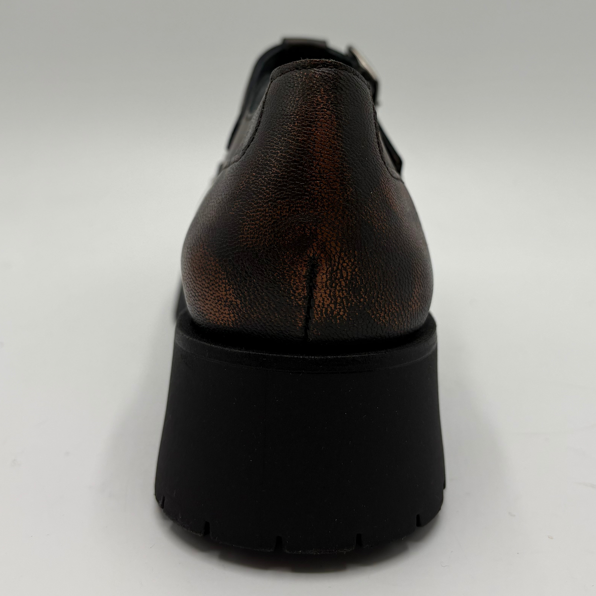 A single brown distressed leather T-strap Mary Jane shoe with silver stud detailing and a black chunky lug sole, shown from the back on a light gray background.
