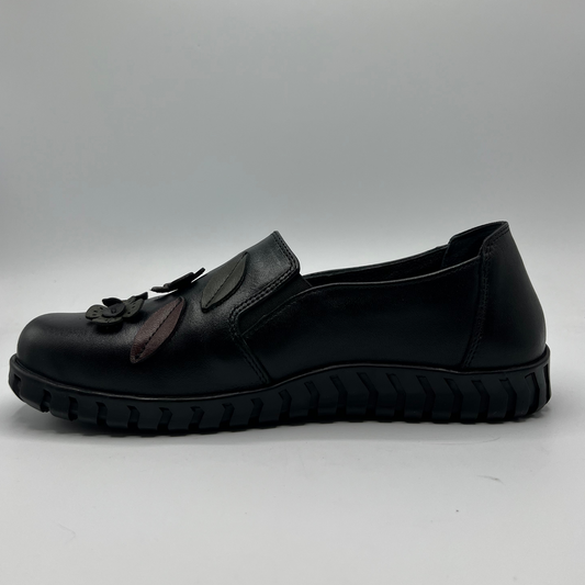 Black slip-on shoe with a decorative element on a gray background
