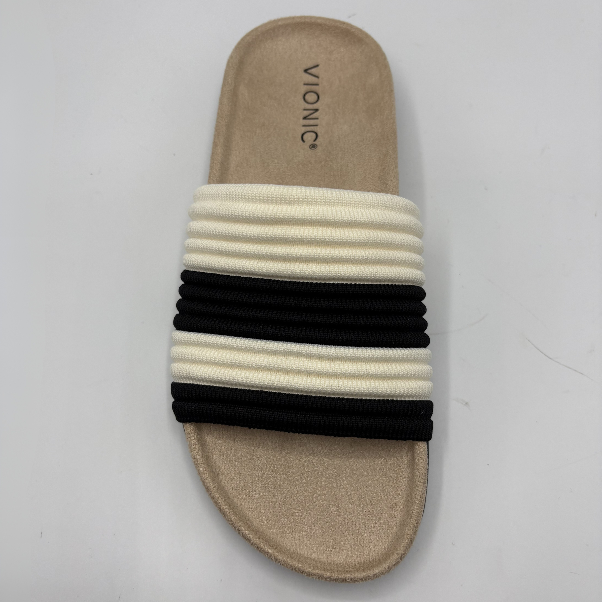 Beige sandal with black and white striped band on a gray background