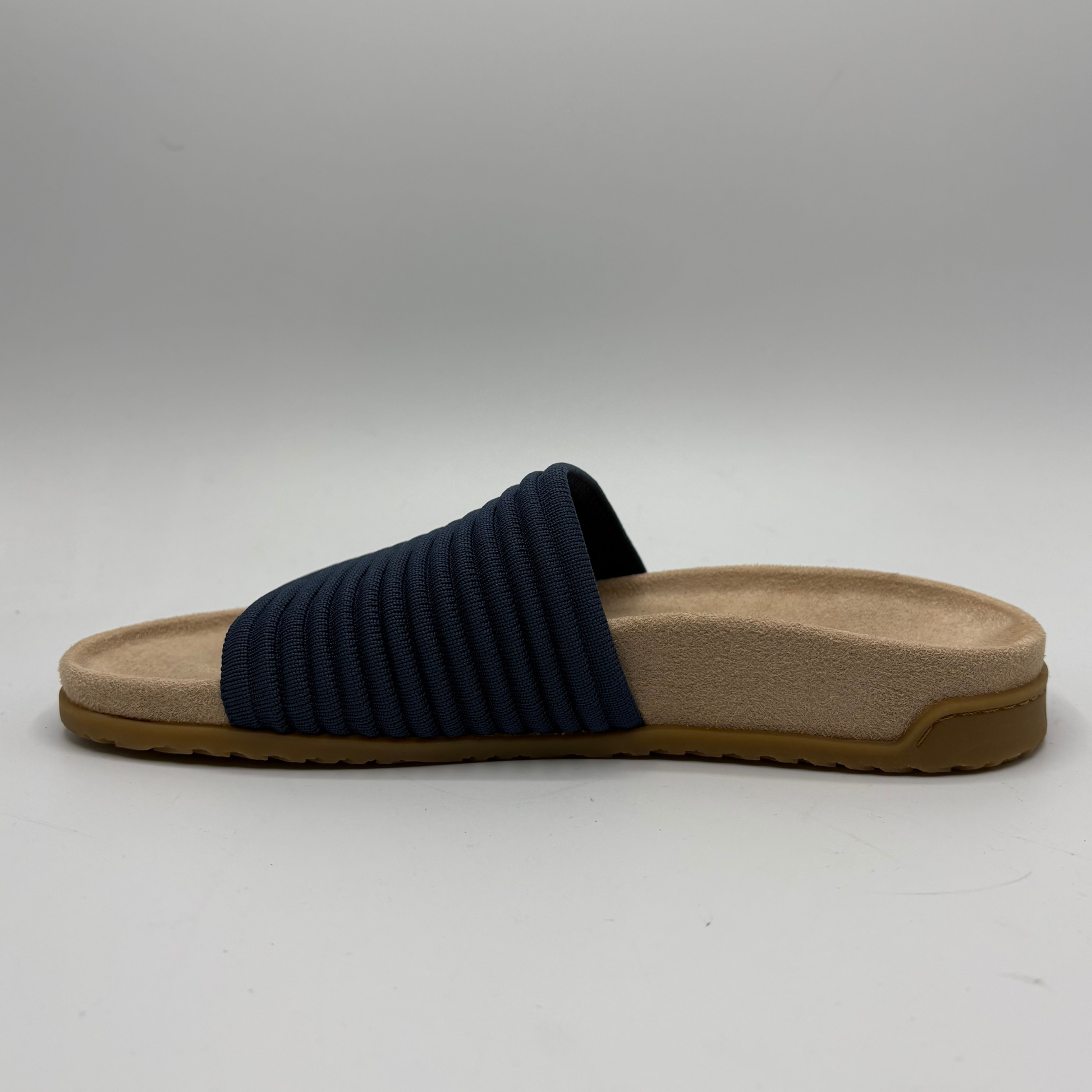 Navy slide sandal with a beige sole on a gray background