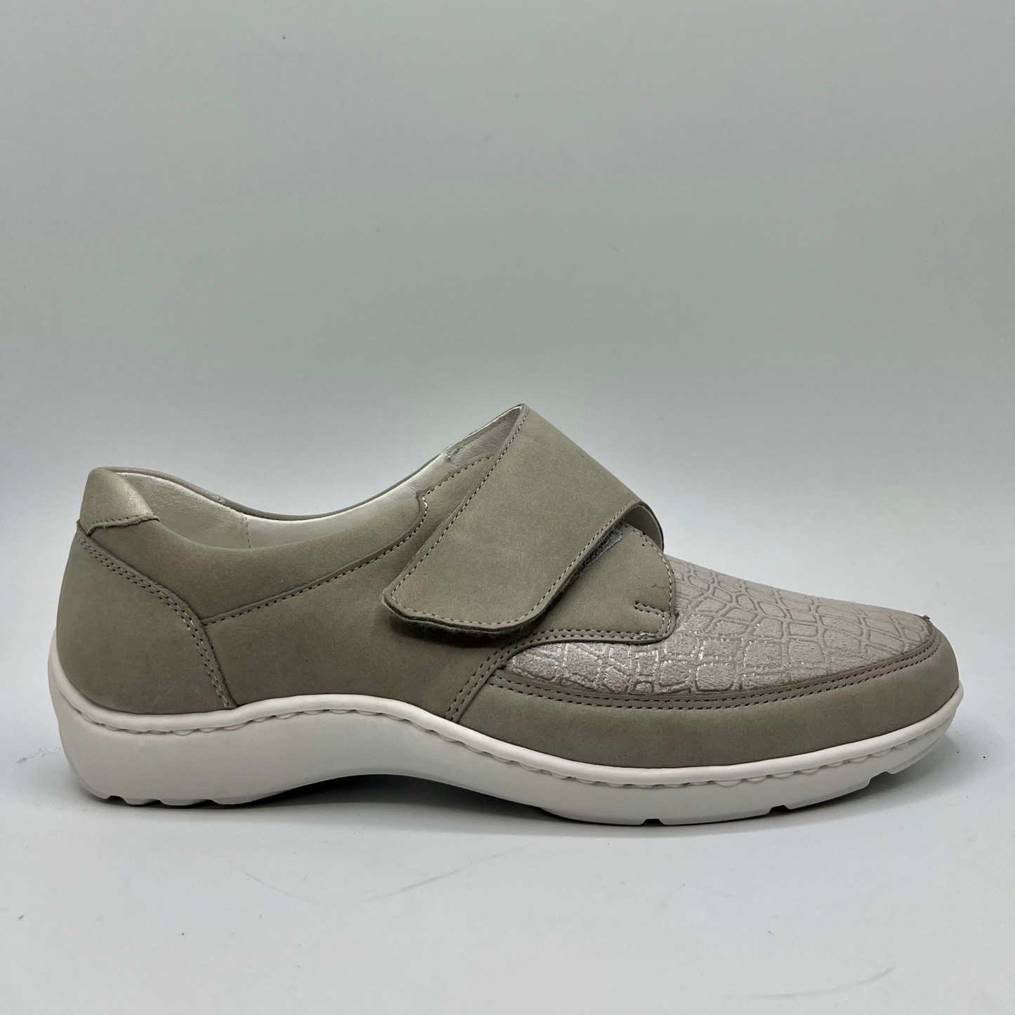 Right facing view of a grey sneaker with a velcro strap and a contoured footbed.