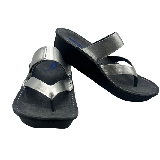 View of a pair of metallic silver sandals with a wedge heel and an adjustable strap