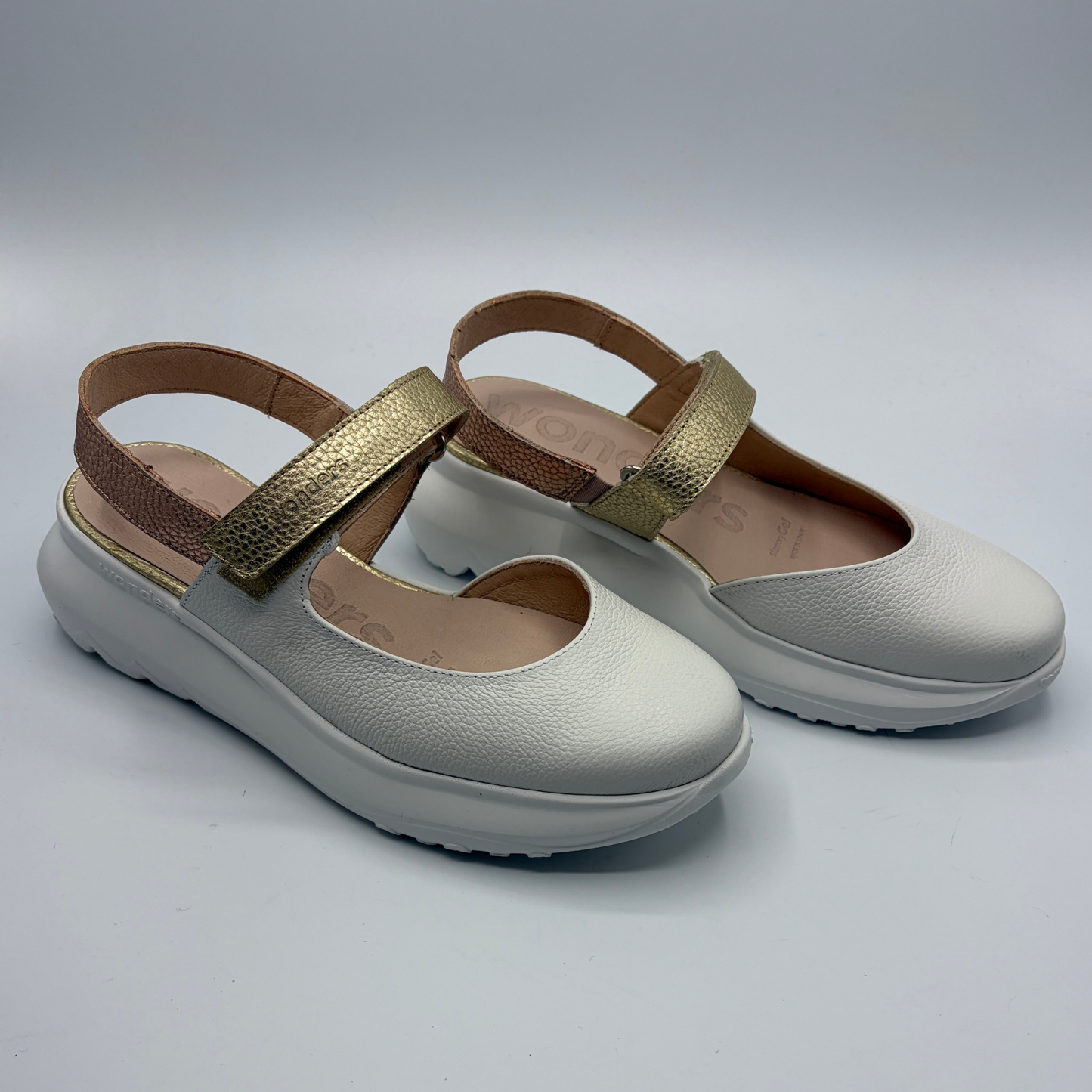 Pair of white shoes with gold straps on a light gray background