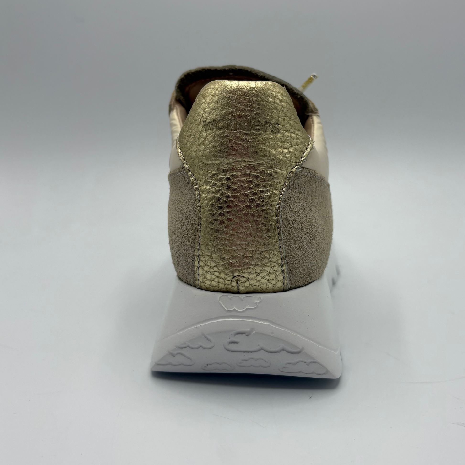 Back view of a sneaker with a textured gold sole on a gray background
