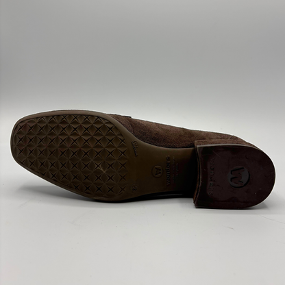 The outsole and heel of a brown suede shoe, showing a textured diamond-pattern tread and a dark brown rubber heel cap with a circular logo, photographed on a light gray background.
