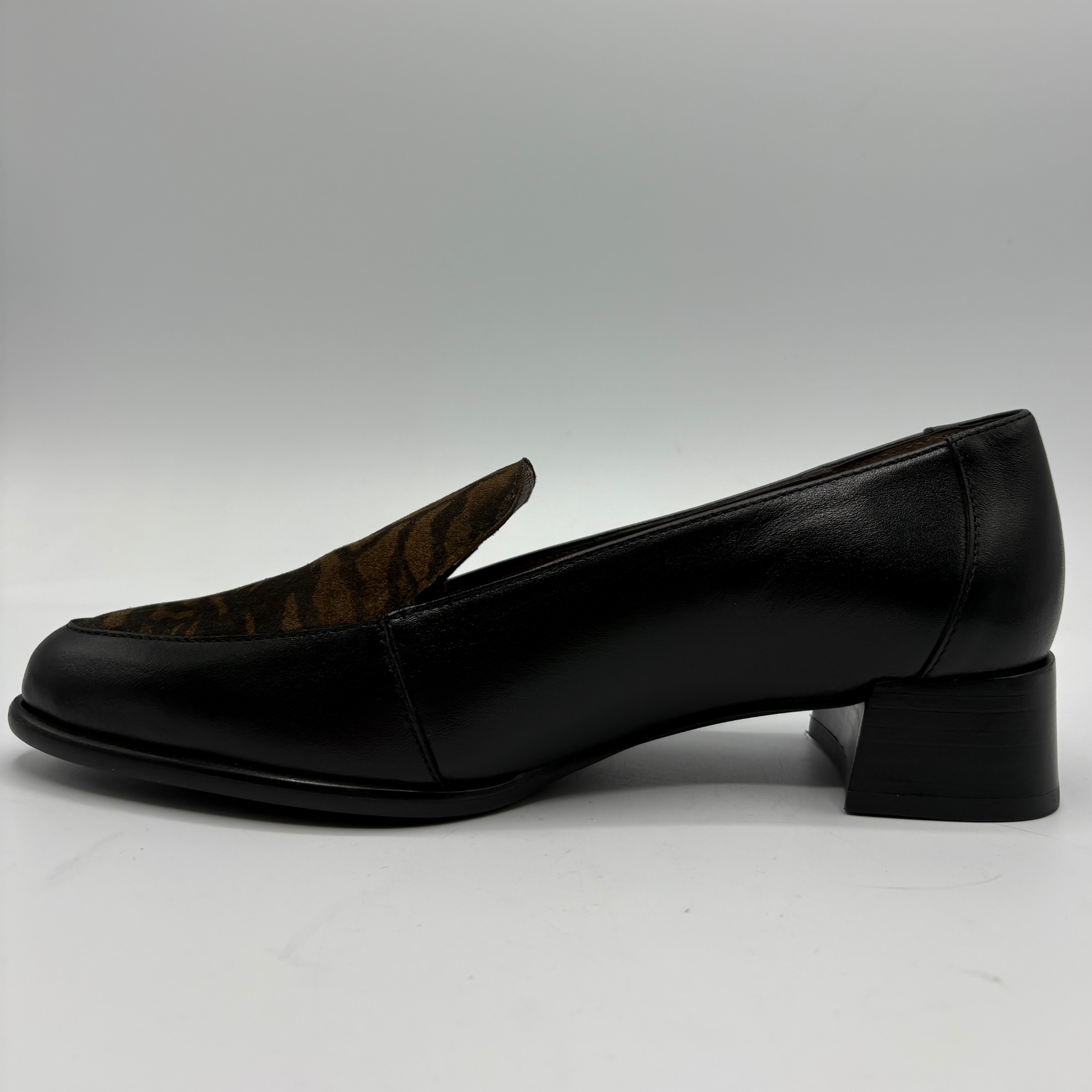 A single black leather loafer-style shoe with a low block heel, shown in side profile against a light gray studio background.