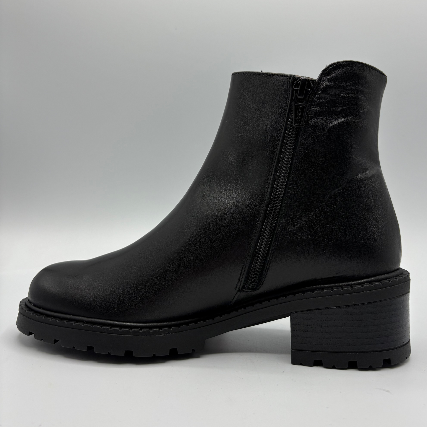 A black leather ankle boot with a side zipper, chunky block heel, and lug sole, shown in profile against a light gray background.