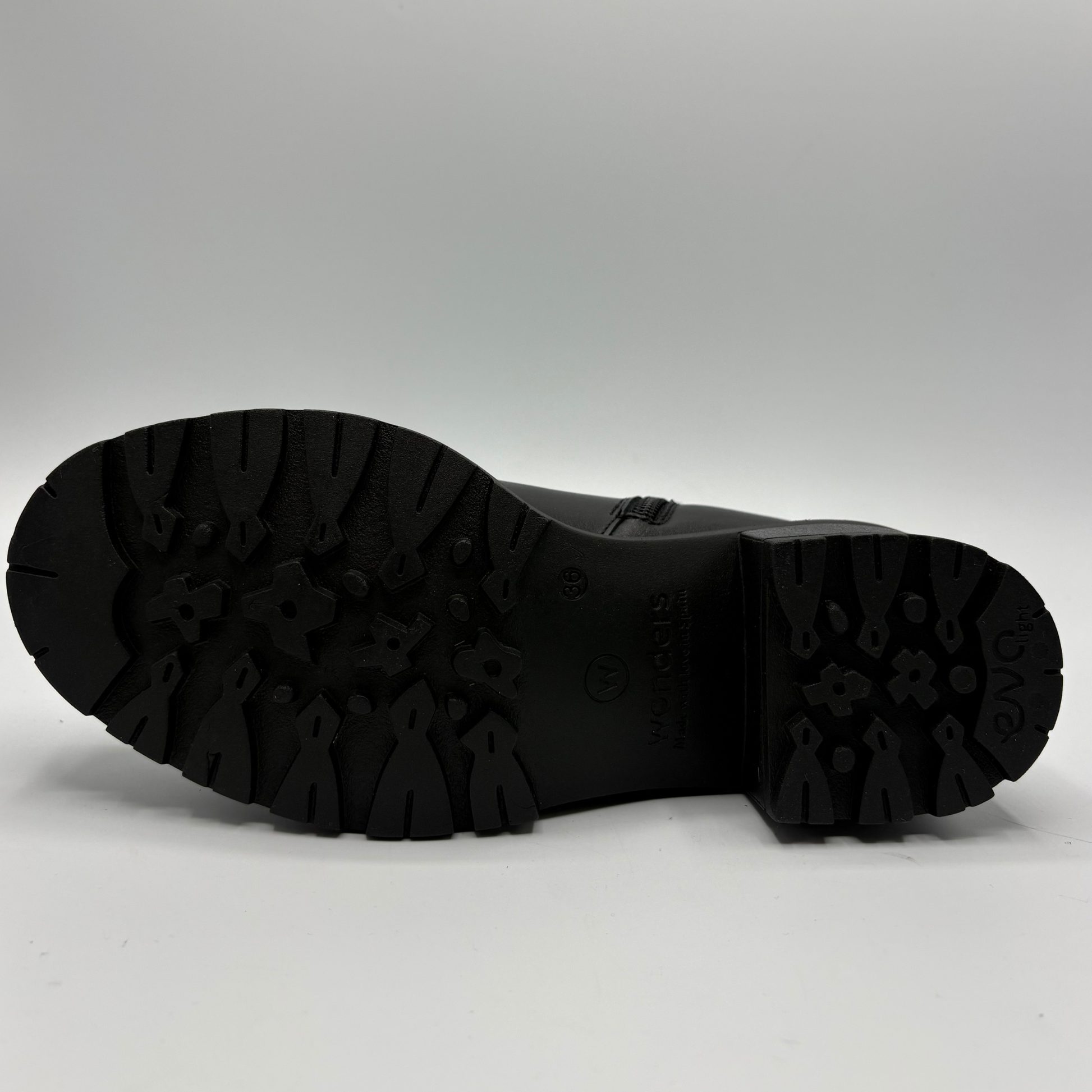 A close-up view of the black rubber outsole of a boot, showing the tread pattern and heel, on a light gray background.