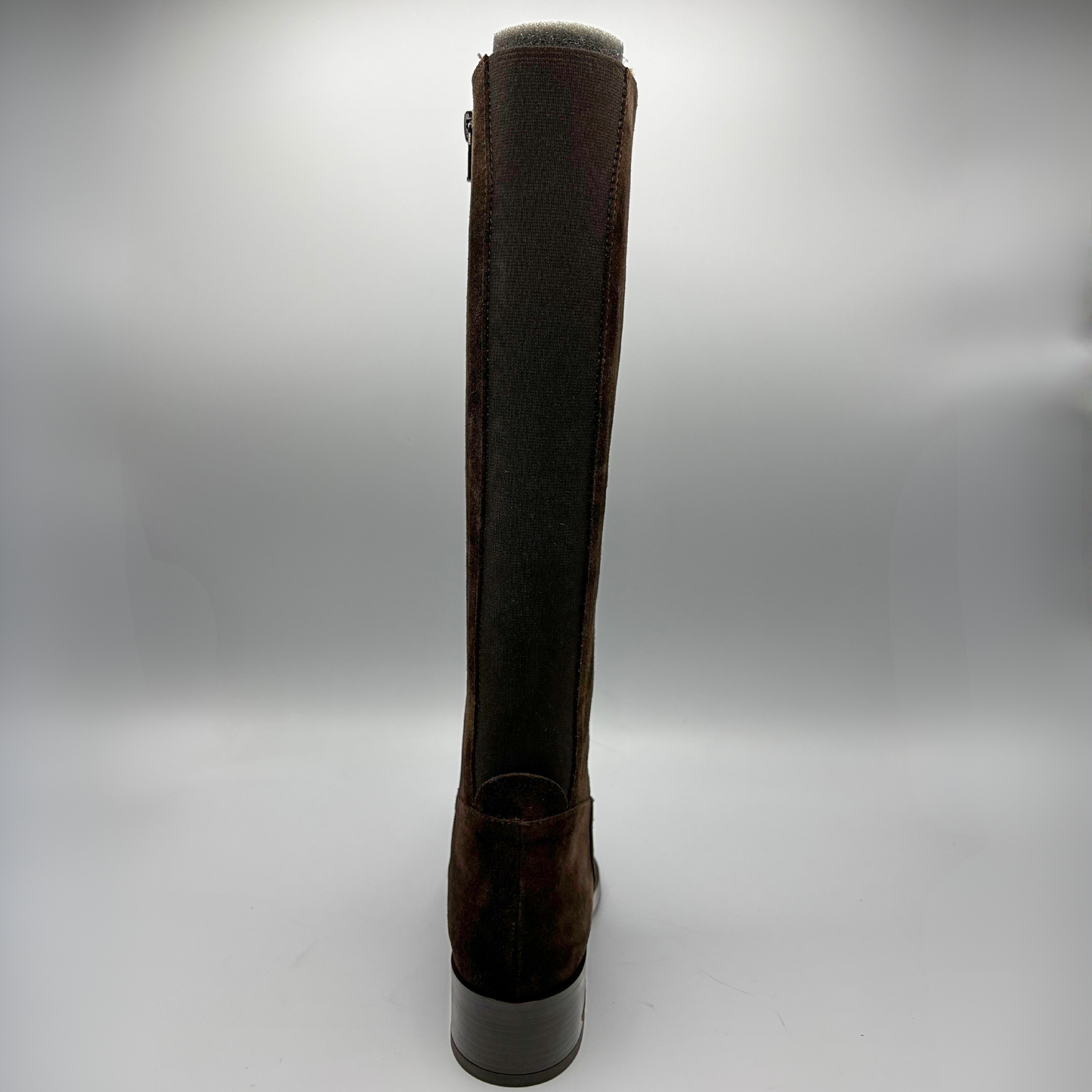 A single knee-high boot shown from the back on a neutral gray studio background. The boot features a dark brown suede-like upper with a contrasting dark gray inner lining and a dark gray block heel.