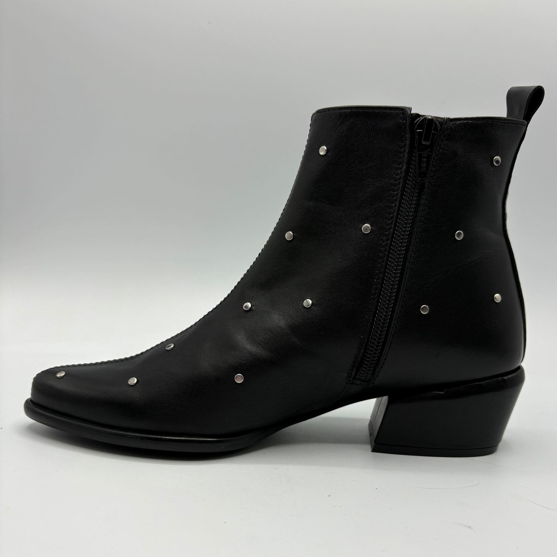 A black leather ankle boot with a low block heel, side zipper, and silver metal studs, shown from a side profile view on a light gray background.