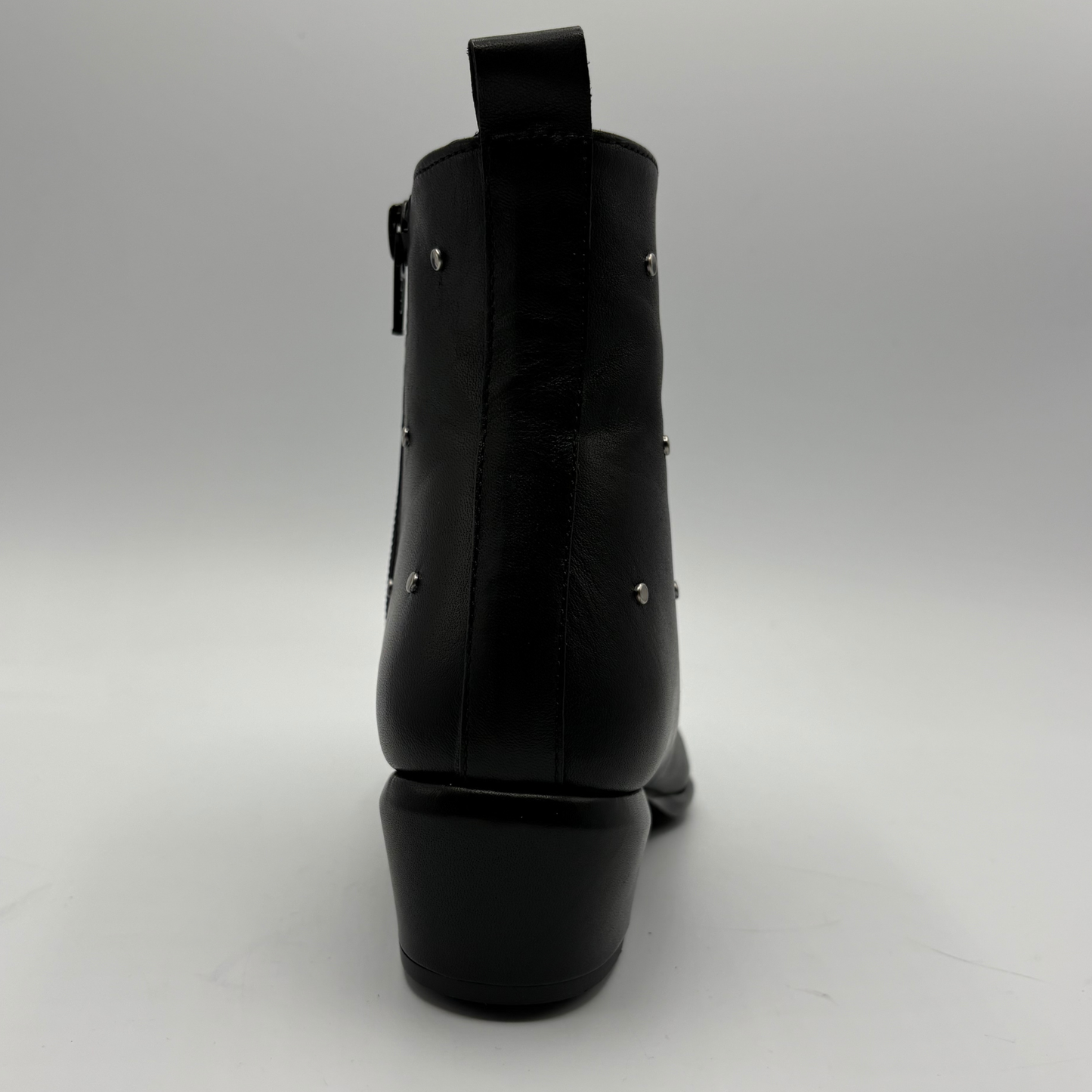 Black leather ankle boot shown from the back, featuring a low block heel, side zipper, and small silver stud embellishments, photographed on a light gray studio background.