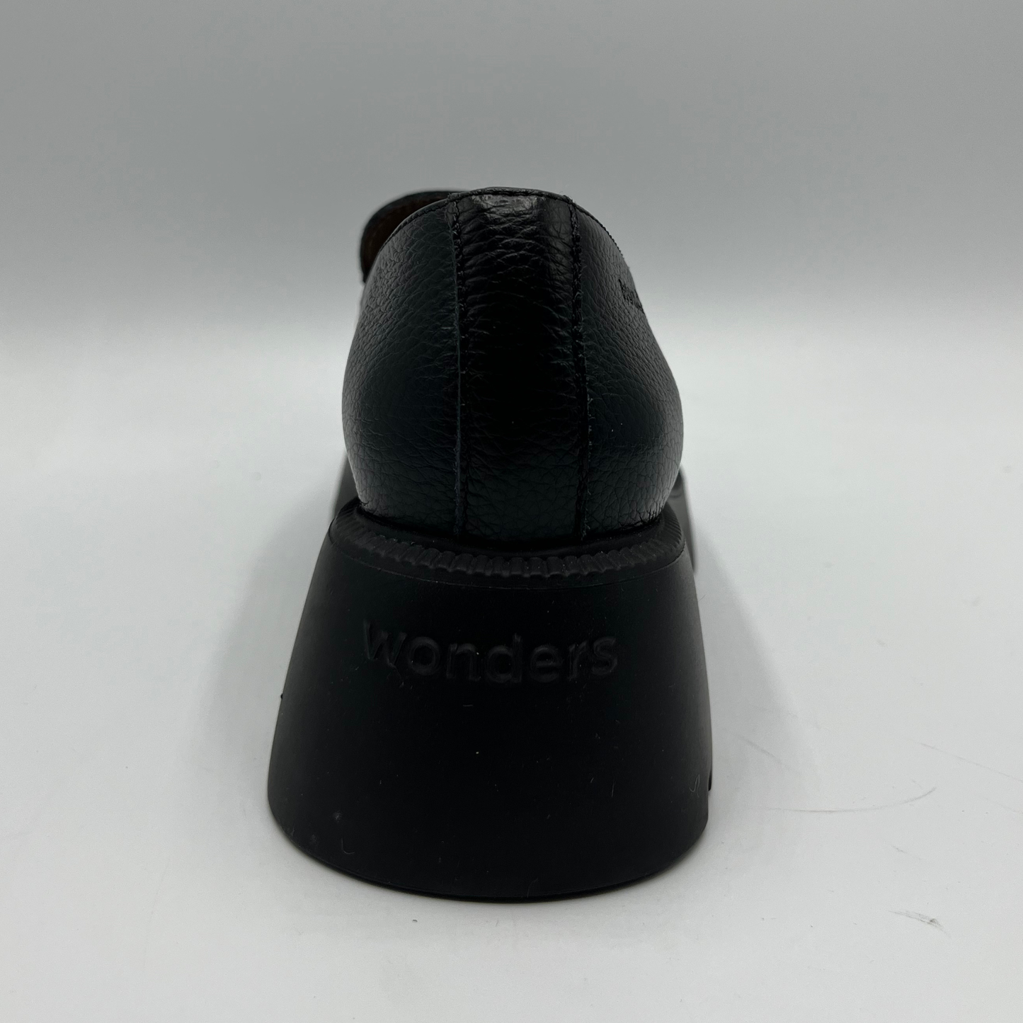 Black shoe on a white stand with 'Wonders' branding on a white background