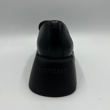 Black shoe on a white stand with 'Wonders' branding on a white background