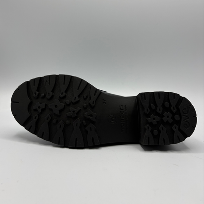 The black rubber outsole of a shoe, showing deep tread patterns and embossed branding, photographed against a neutral gray background.