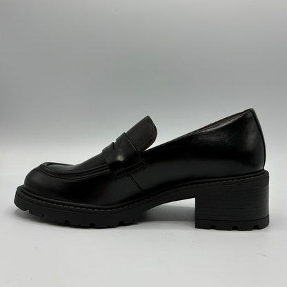 A single black leather penny loafer with a chunky block heel and lug sole, shown in a side profile against a neutral gray background.