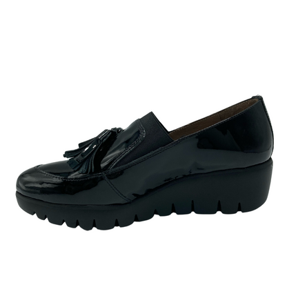 Left facing view of black patent leather loafer with wedge sole and tassel detail on toe box