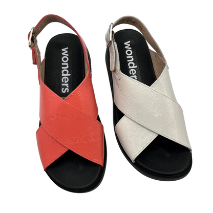 Top view of two leather sandals side by side. One is coral and one is white, both have a black outsole and contoured footbed. Adjustable slingback strap.