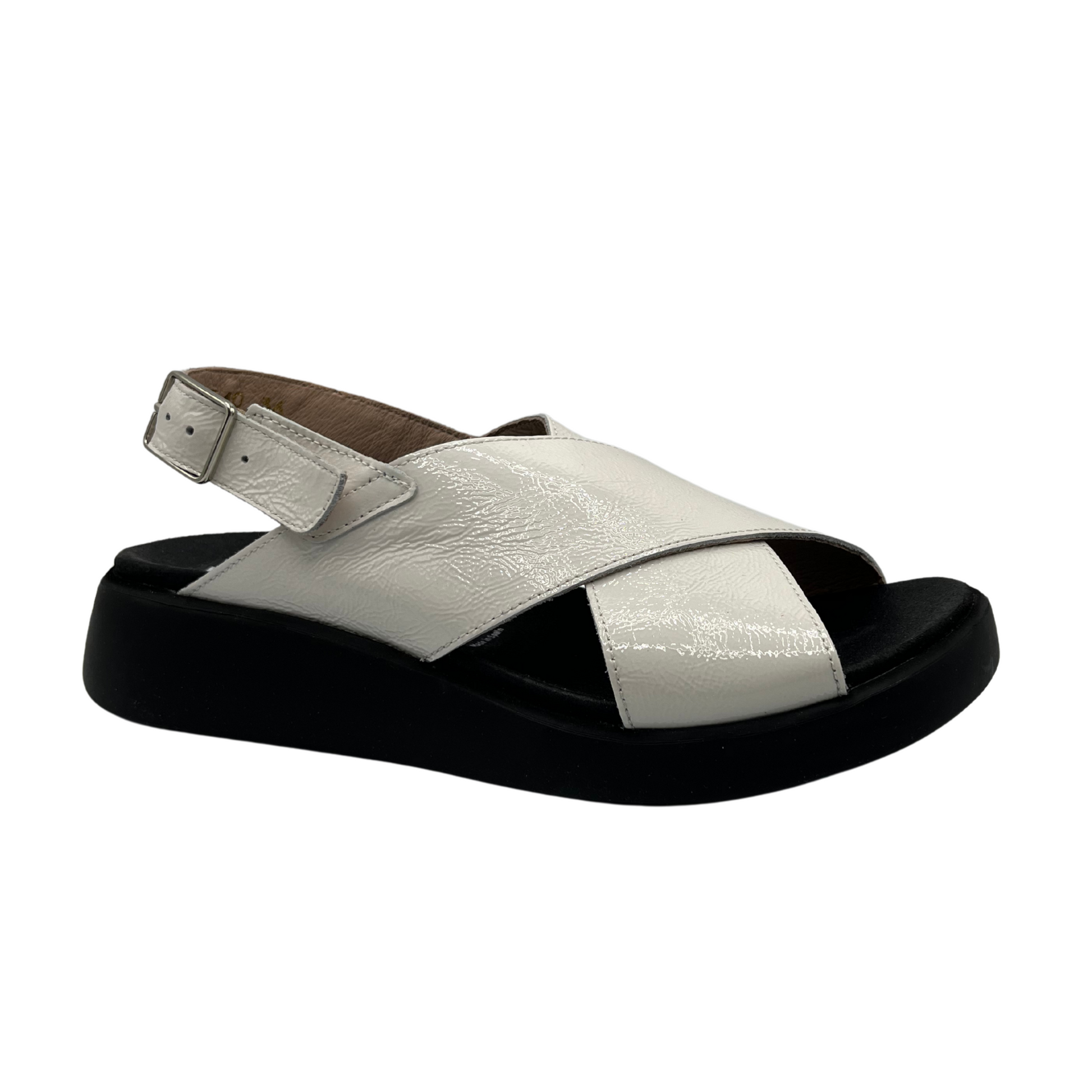 Angled view of white coloured leather sandal. Black outsole with a contoured footbed and adjustable slingback strap.