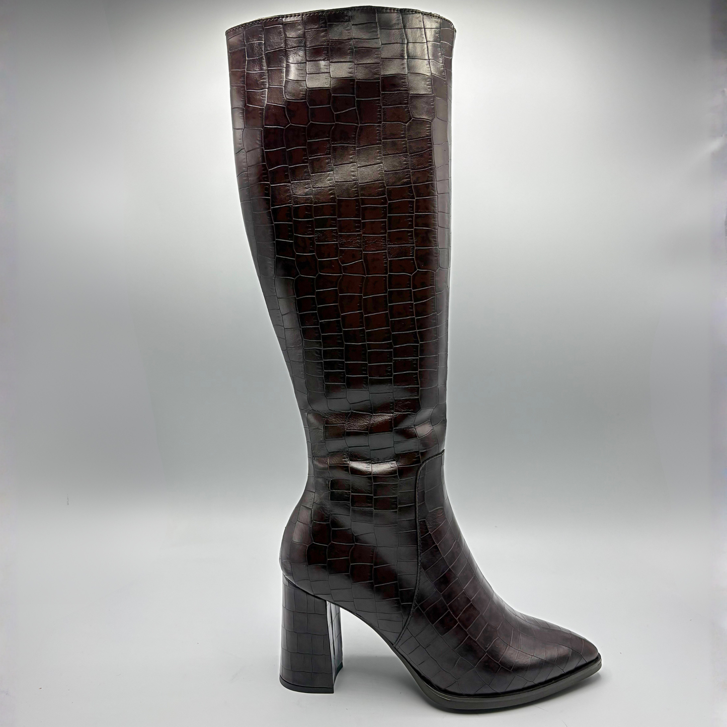 A single knee-high boot in glossy dark brown crocodile-embossed leather, shown from the side against a neutral gray studio background.
