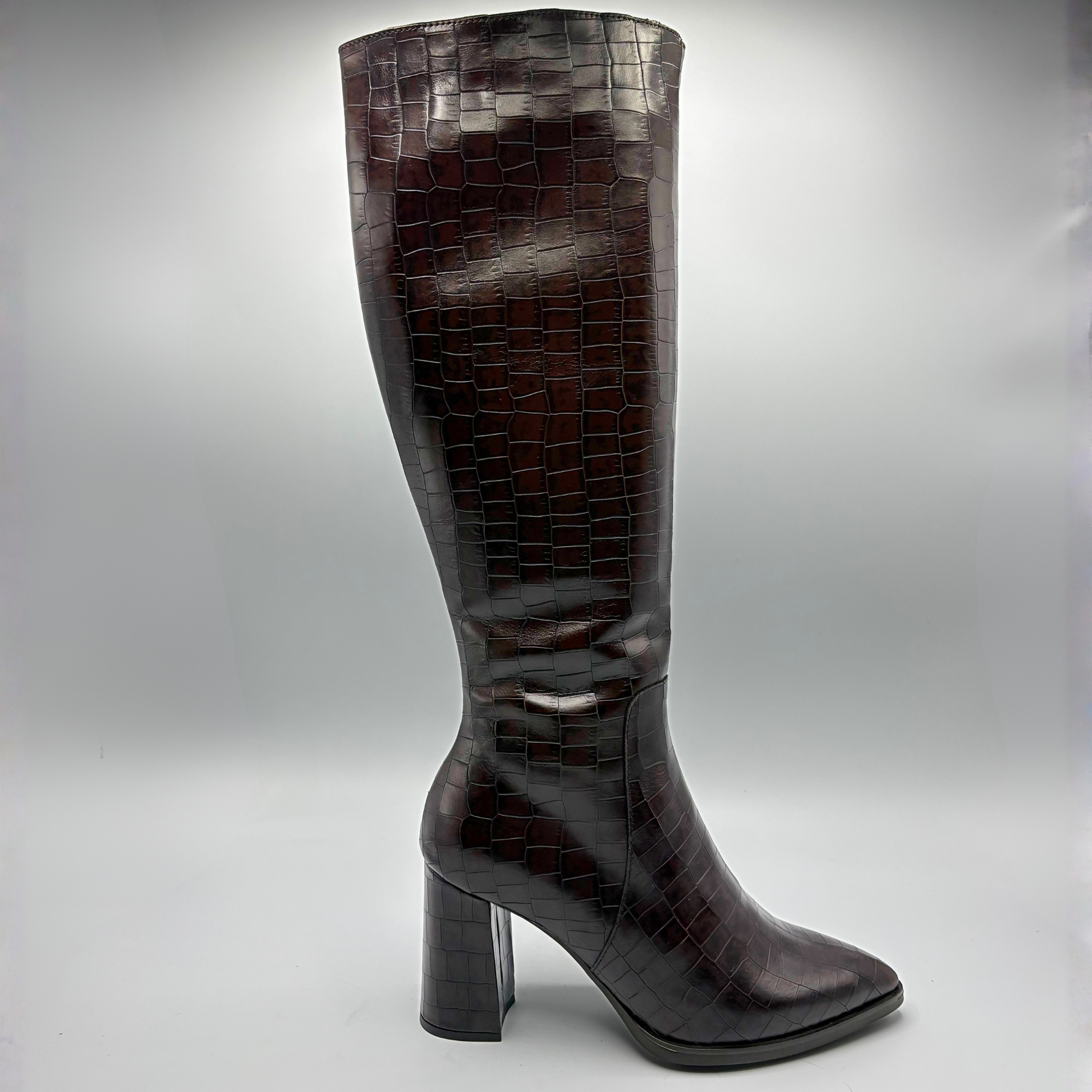 A single knee-high boot in glossy dark brown crocodile-embossed leather, shown from the side against a neutral gray studio background.