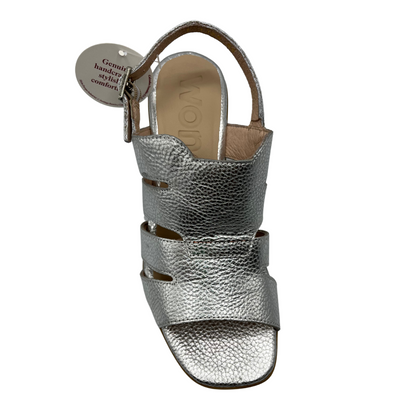 Top view of a leather sandal in a silver colour with an open toe and adjustable slingback strap. Featuring a chunky block heel in a wood grain.