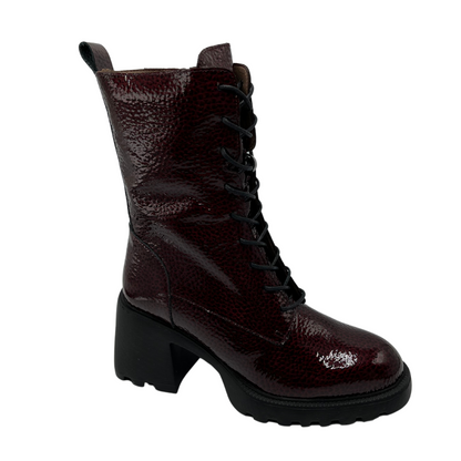 45 degree angled view of dark wine coloured patent leather boot. Black lace up closure, chunky black outsole and heel.