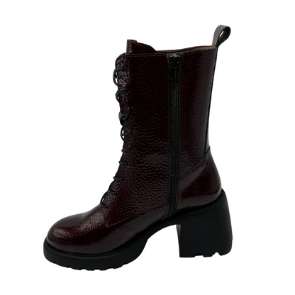 Left facing view of dark wine coloured patent leather boot. Black lace up closure, chunky black outsole and heel.