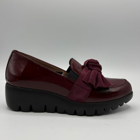 A single women's slip-on platform shoe in deep burgundy, featuring a glossy patent leather upper, a matching fabric bow detail on the side, and a chunky black platform sole.