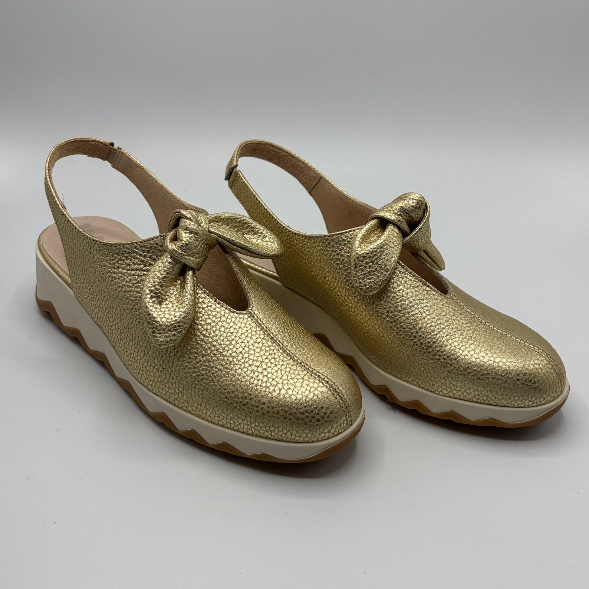 Pair of gold shoes with bow details on a white background