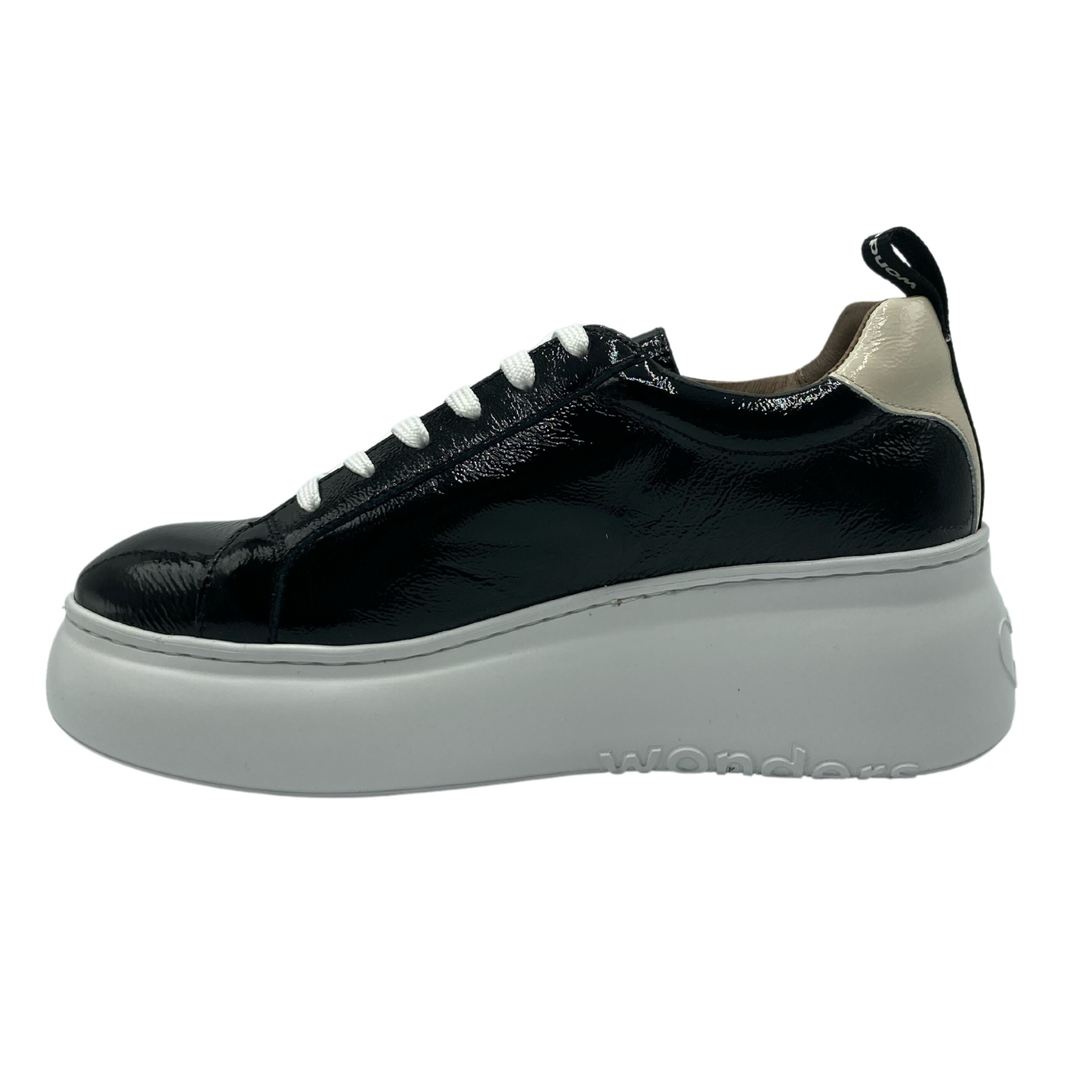 Pictured is a black patent leather sneaker on a white platform sole in left profile. The sneaker has white lace up detail and a cream patent detail on the heel.