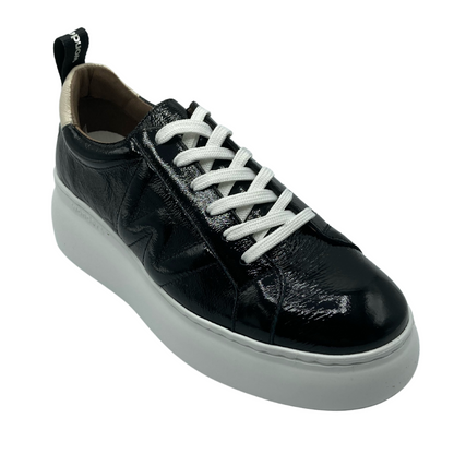 Top down angled view of a black patent sneaker with a white platform sole and cream patent detailing on the heel. This sneaker laces up with white lacing.