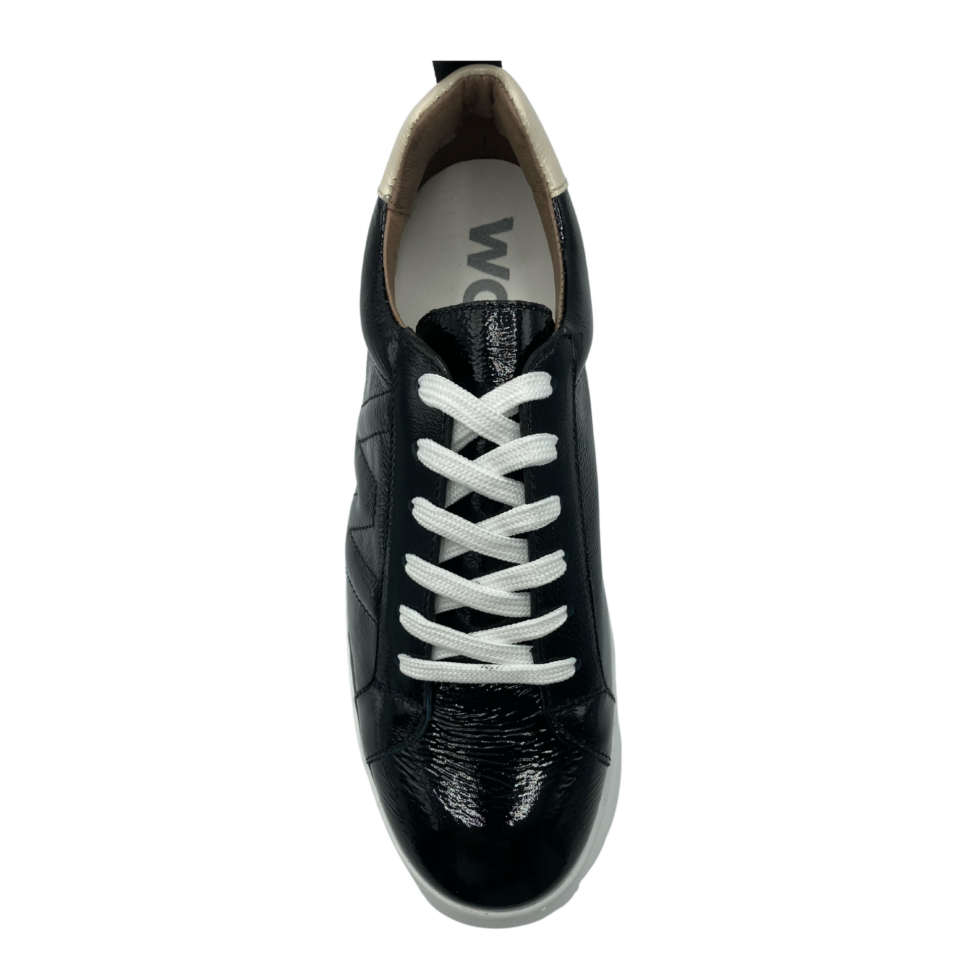 Top view of a black patent sneaker on a white platform sole. The sneaker has white lacing. 