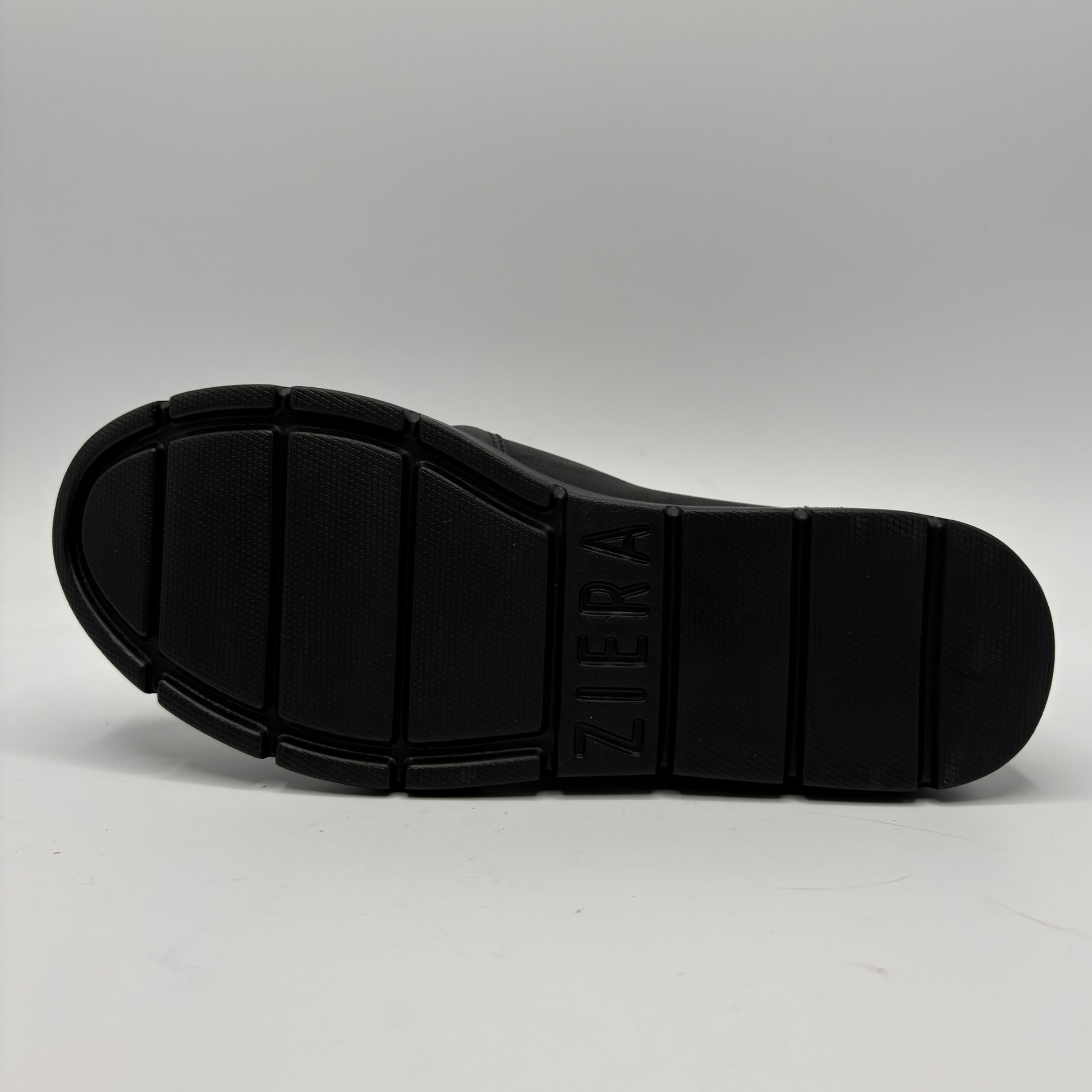 The black rubber outsole of a ZIERA shoe, showing the brand name embossed vertically on the rear section, photographed against a neutral gray background.