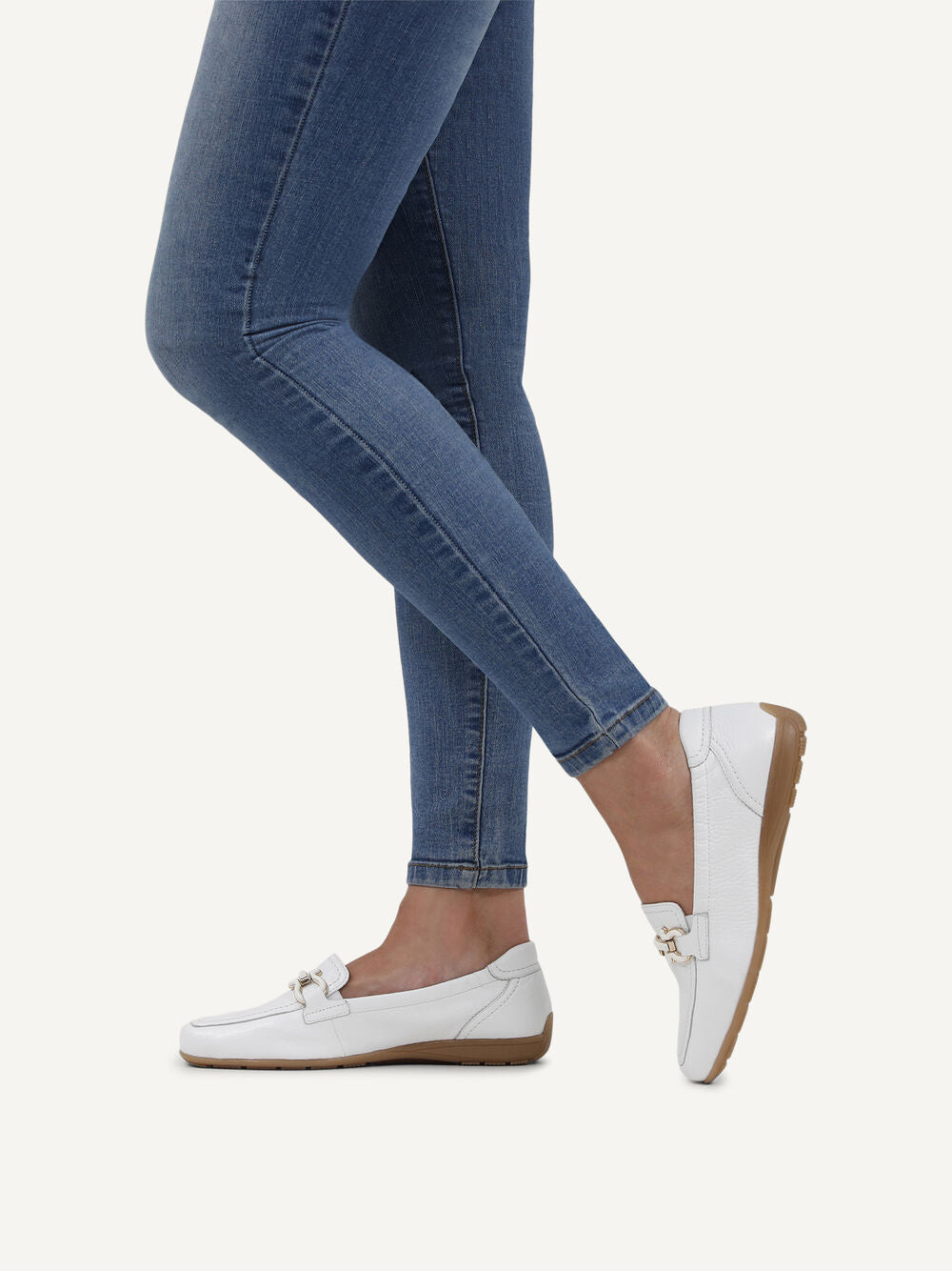 Person wearing blue jeans and white loafers on a light gray background