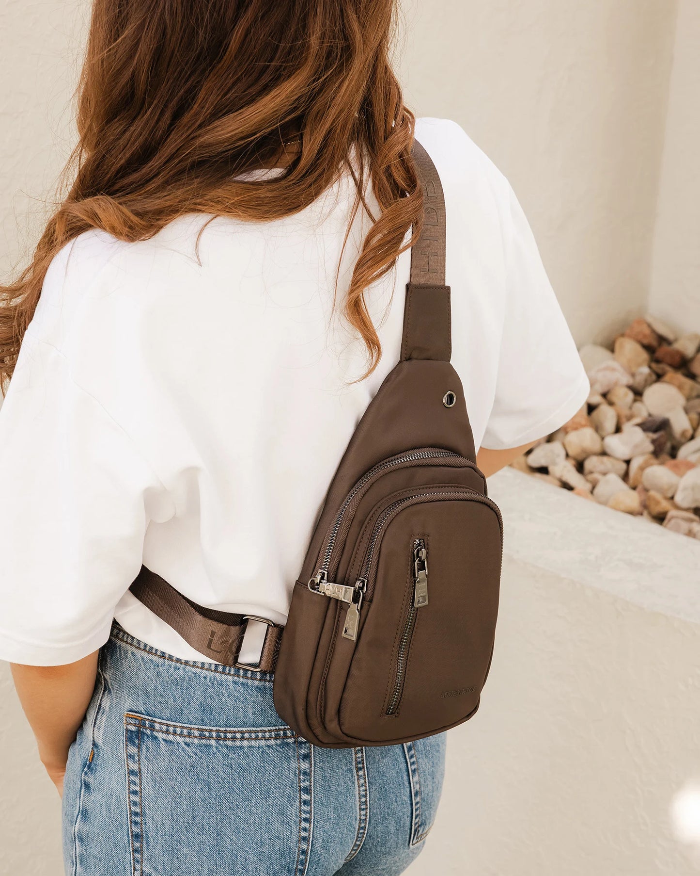 Person wearing a brown sling bag over one shoulder with a neutral background