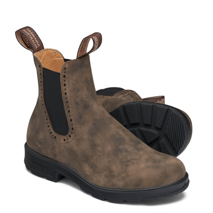 A pair of smokey brown leather boots with black soles. Black elastic sides surrounded by broguing detail.