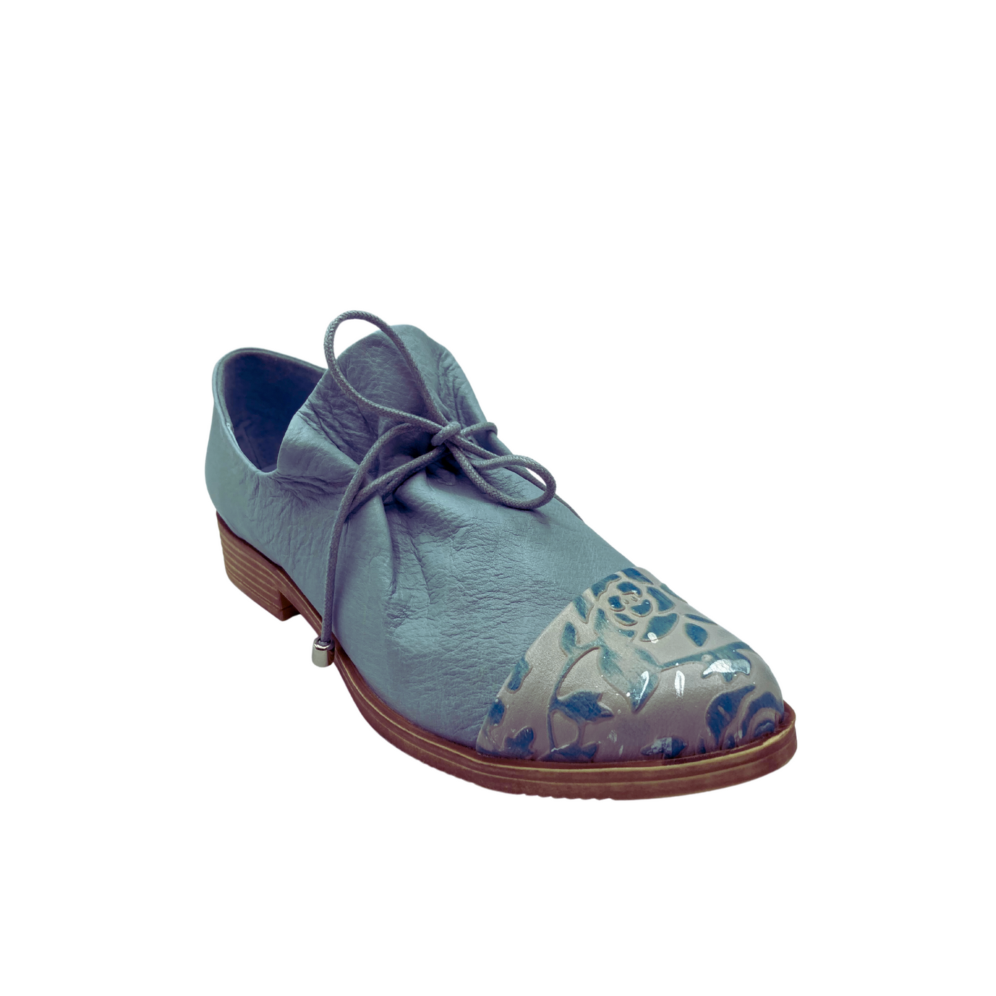 Angled front view of a special little loafer.  Done in a denim blue color with a toe cap in an embossed blue/silver floral.  Laces in front to tighten fit and pull the ruched leather tongue together.