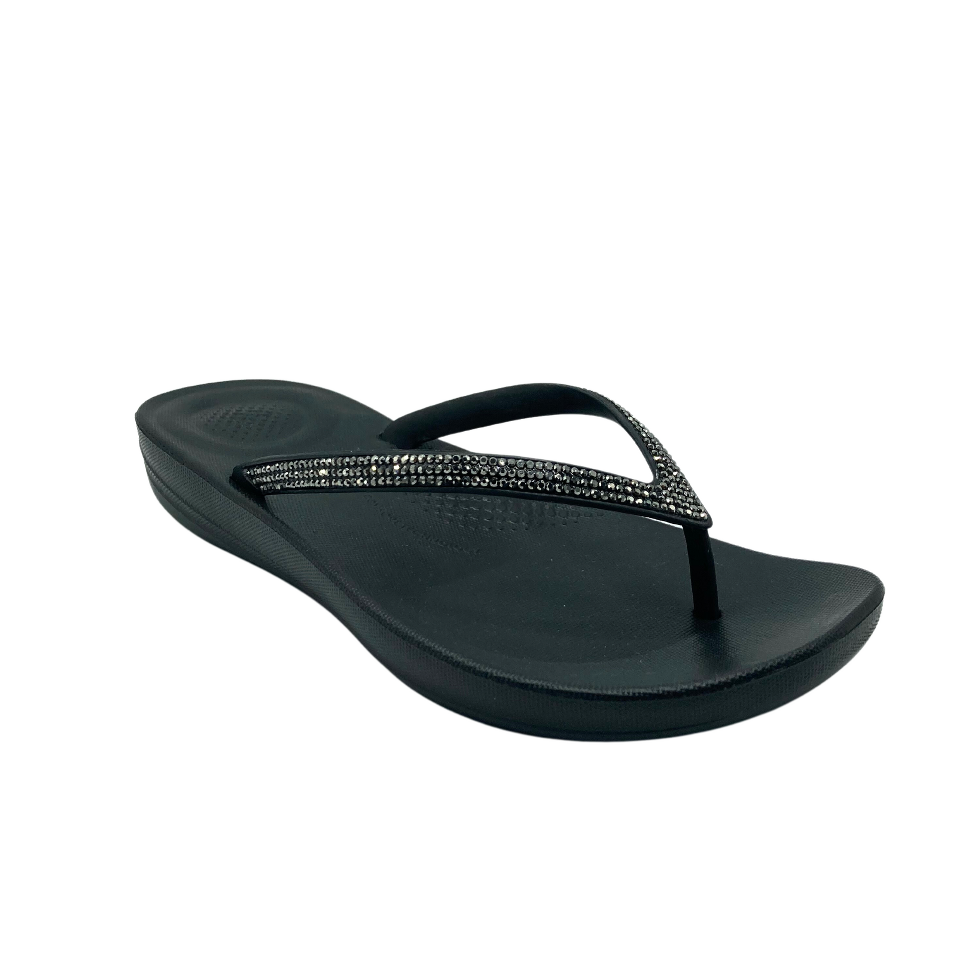 Angled front view of a black Fit Flop sandal with toe post.  Straps have crystals in them.  Ergonomic footbed