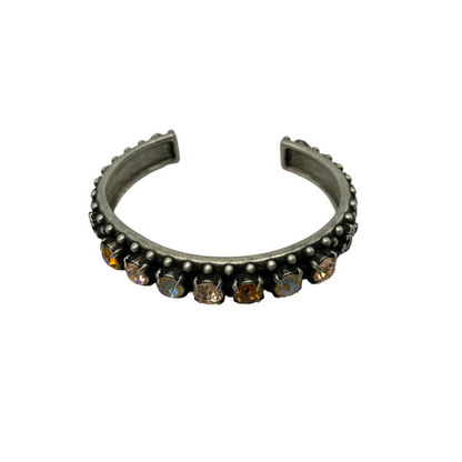 A cuff style bracelet is pictured in silver with a band of assorted stones ranging from pearlescent, to amber, to topaz.