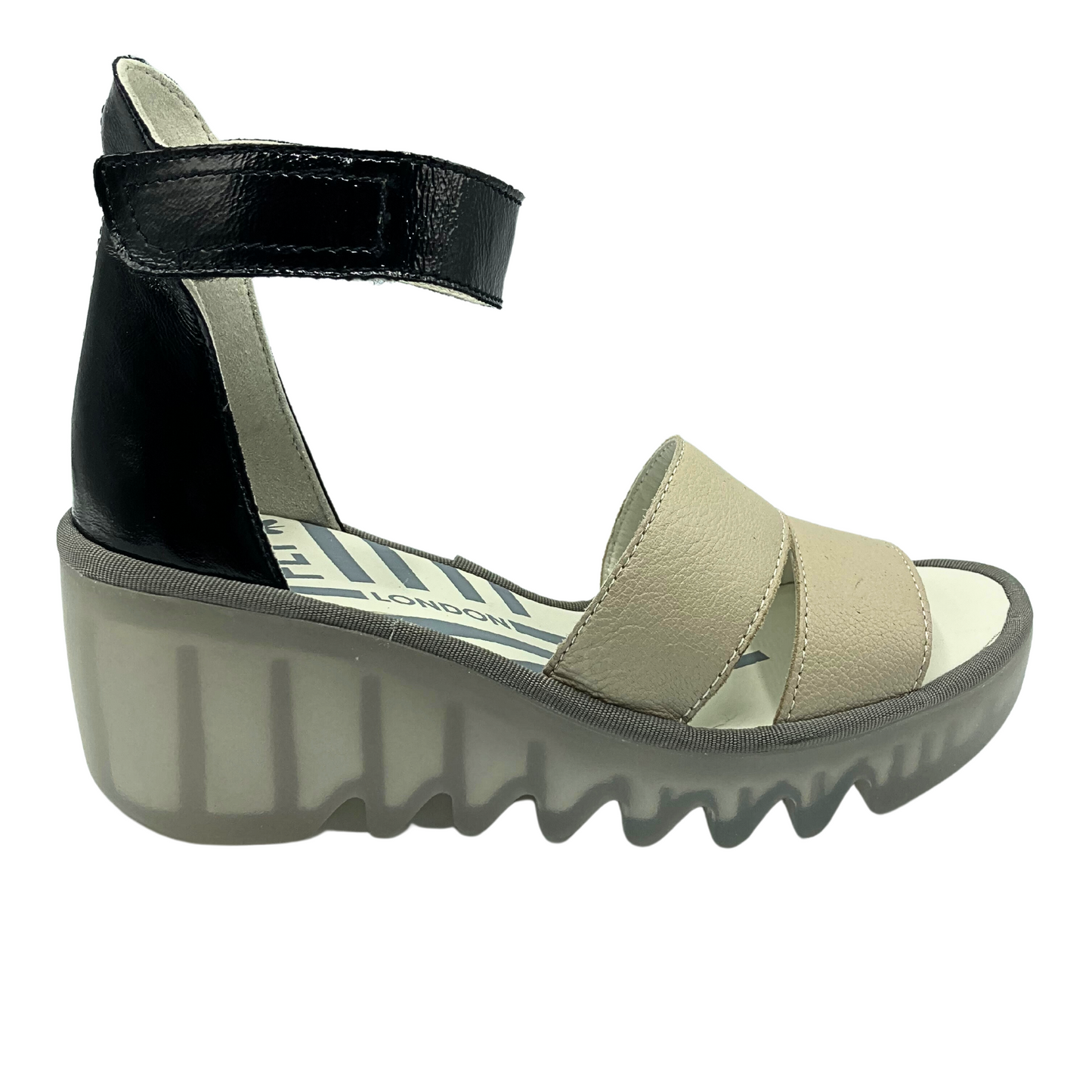 Outside view of a lower wedge Fly London sandal.  Two-tonw with black heel cup and ankle strap and cream straps in front.