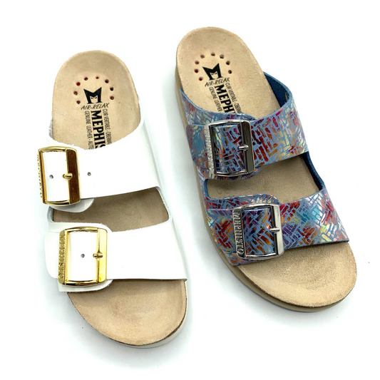 One white patent leather sandal beside a multicoloured sandal. The white version has shiny gold buckles and the multicoloured one has a shiny silver buckle.