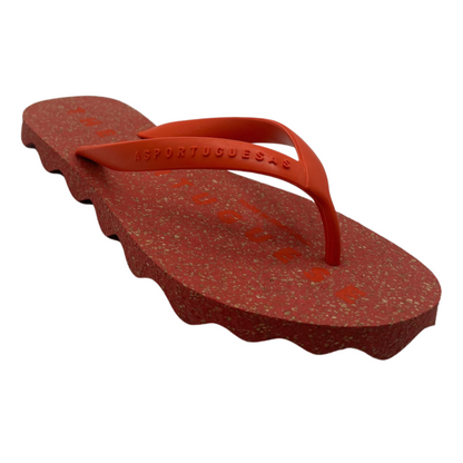 A red speckled flip flop with Y shaped red strap and scalloped sole is pictured at an angle.
