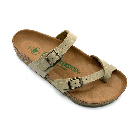 A 45 degree angle view of a sandal with a caramel-brown cork sole, two light-khaki straps, and brushed nickel buckles. One of the straps goes over the upper part of the foot, and the other goes between the toes.