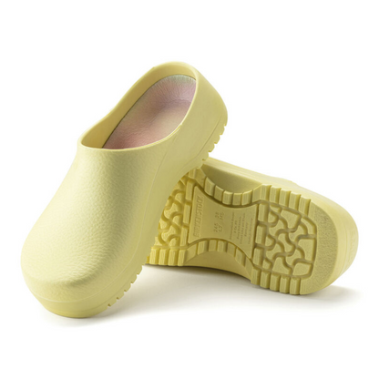Two pale yellow clogs with grippy bases and colourful insoles, one leaning against the other, and the other on its side.