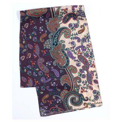 A view of a purple and cream paisley printed scarf lies folded with a detailed view of teal, navy, red, and purple colouring.