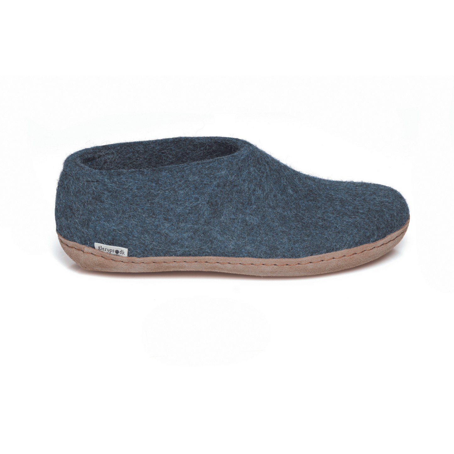 A dark denim-blue slipper is pictured in profile, showing the high back of the heel. The bottom lined in tan leather has a small tag with the brand name attached in the seam where the leather meets the felted wool.