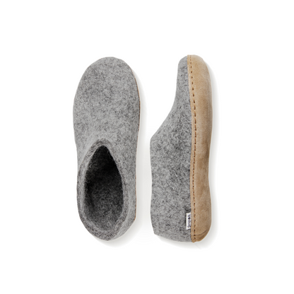 An overhead view of two light grey felted wool tall-back slippers. One is pictured straight on, showing the top face of the slipper, while the other lays on its side, showing the profile with tan leather sole with a row of stitching.