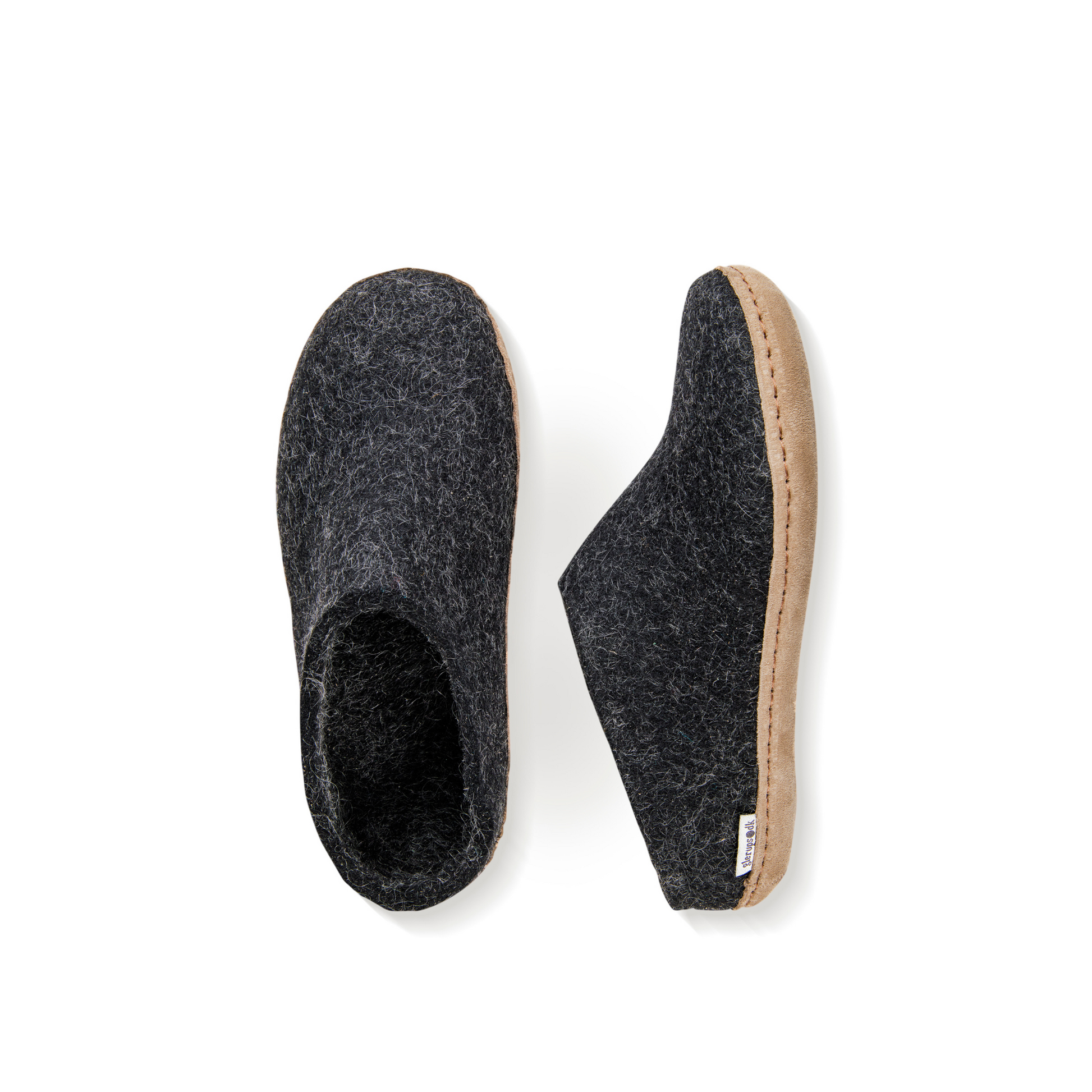 An overhead view of two dark grey felted wool slippers. One is pictured straight on, showing the top face of the slipper, while the other lays on its side, showing the profile with tan leather sole with a row of stitching.