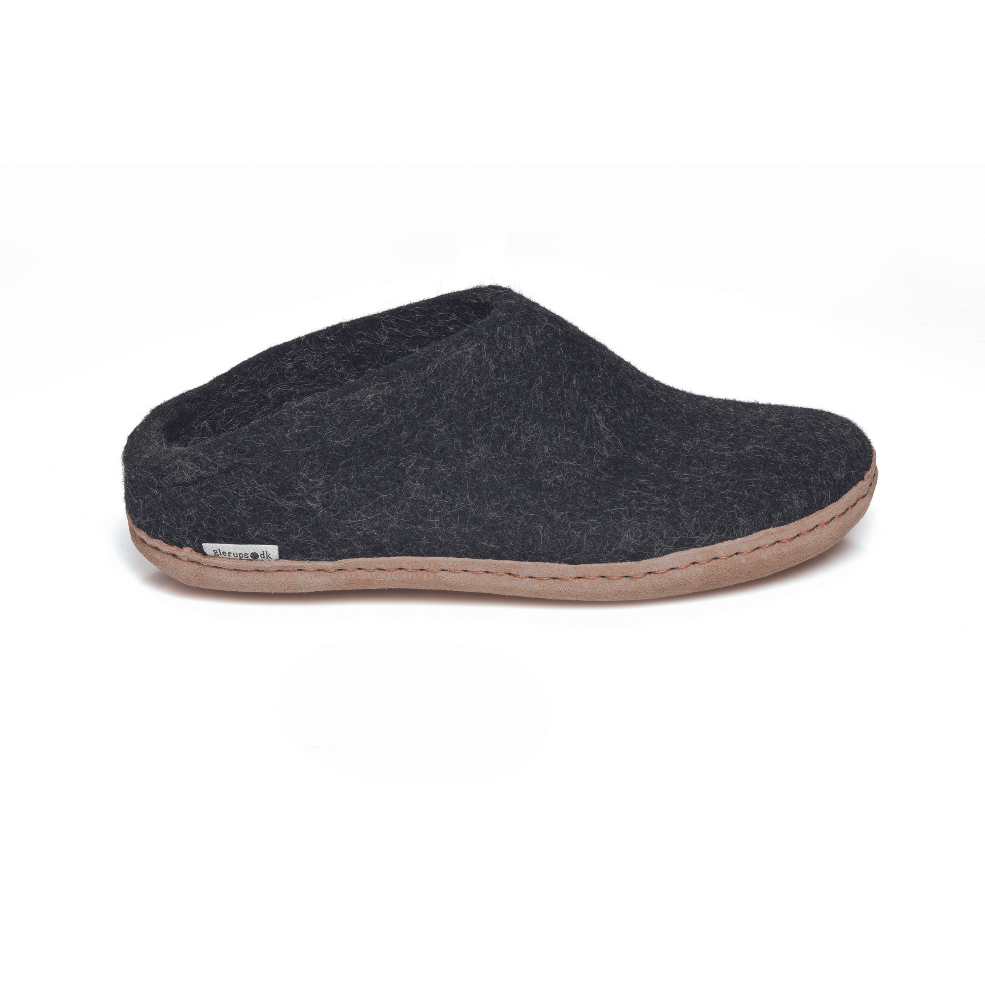 A dark grey slipper is pictured in profile, showing the low back of the heel. The bottom lined in tan leather has a small tag with the brand name attached in the seam where the leather meets the felted wool.